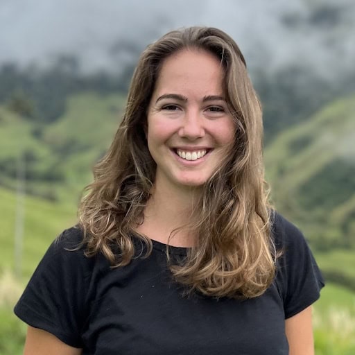 Woman smiling outdoors in front of hilly landscape.