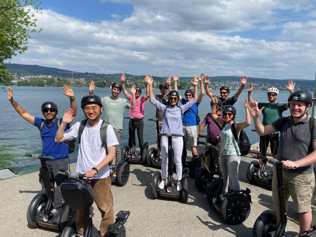 Gruppe auf Segways am Seeufer winkt.