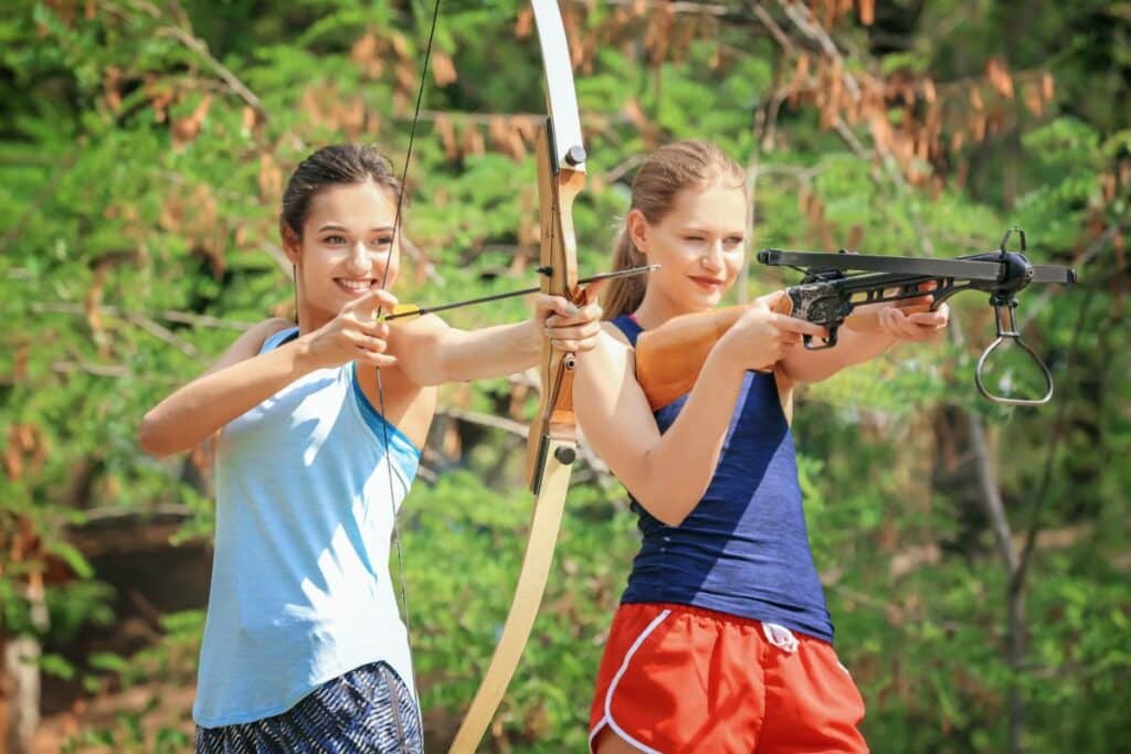 Zwei Frauen zielen mit Bogen und Armbrust.