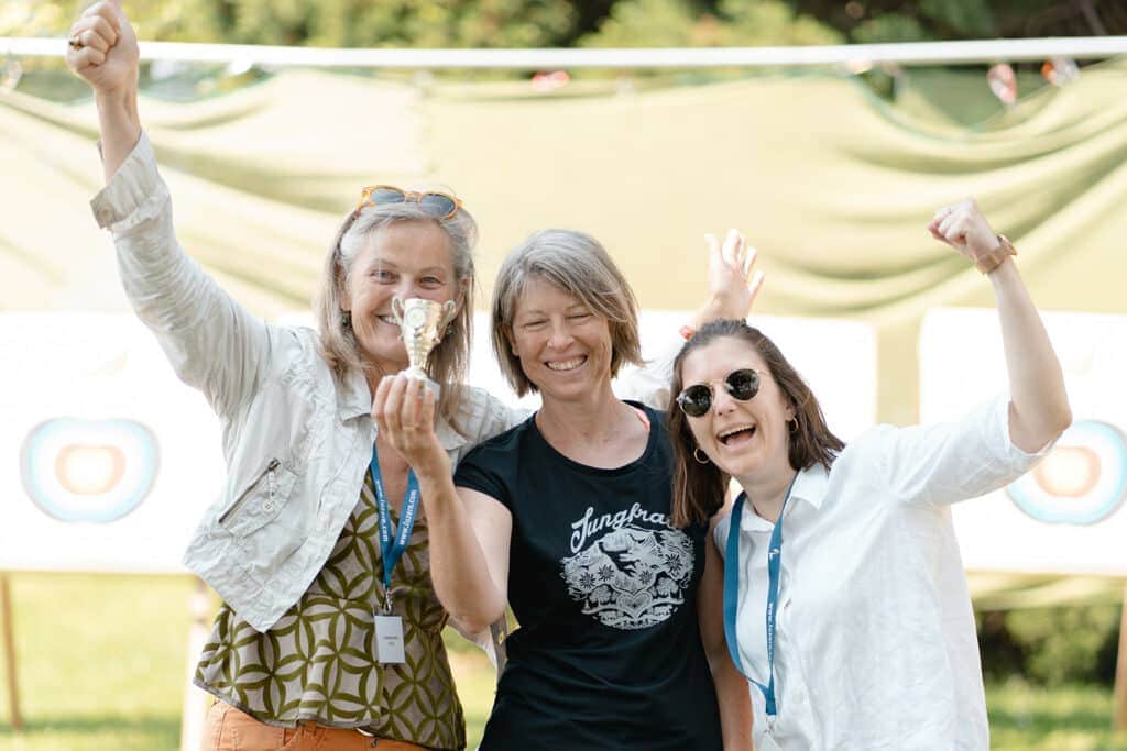 Three smiling women with trophy and raised arms.