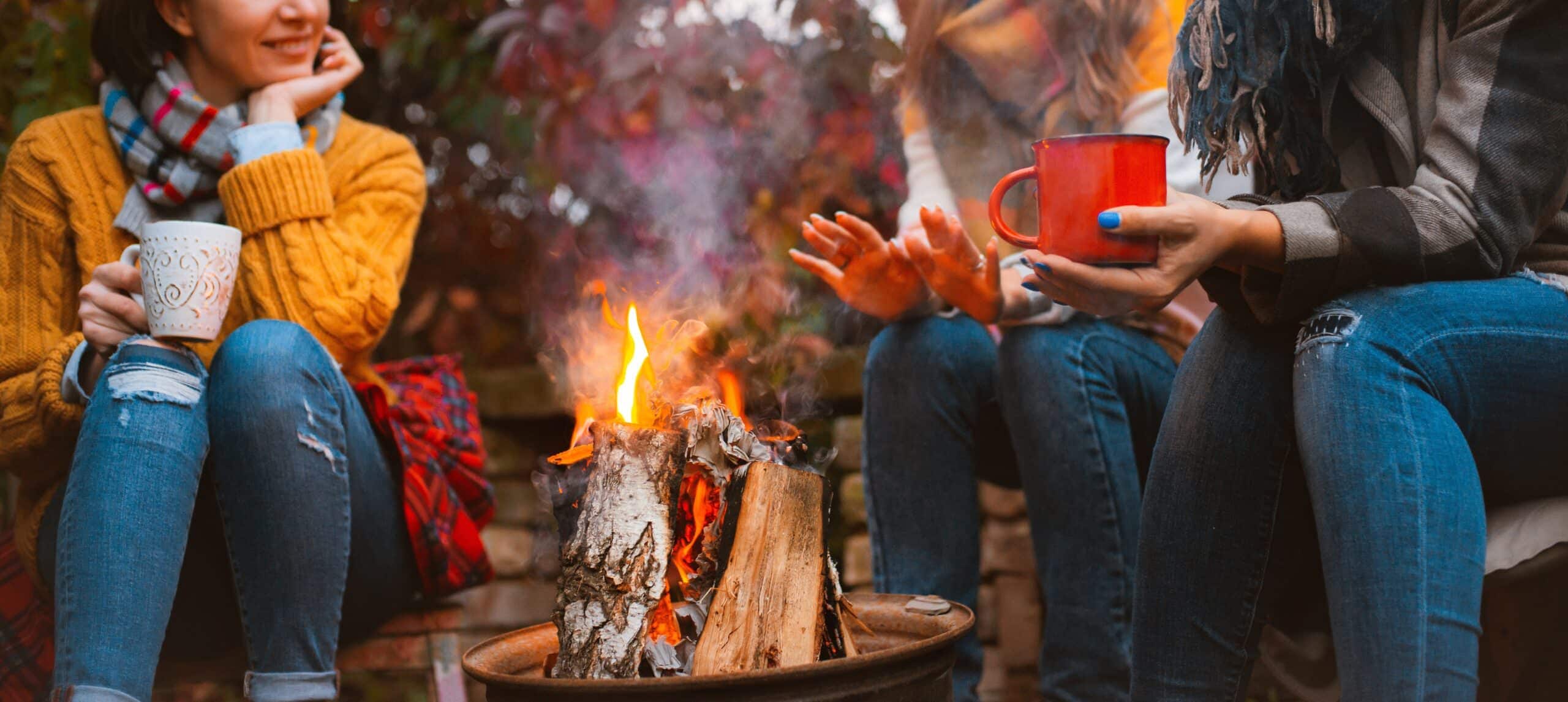 Friends enjoying campfire and hot drinks outdoors.