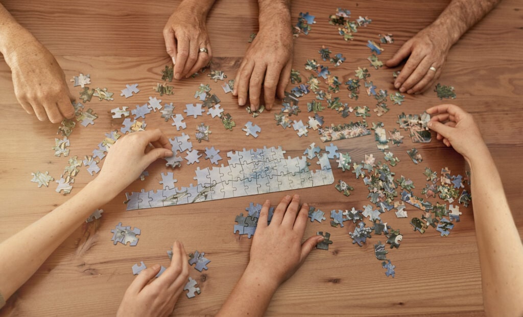 Hände legen Puzzle zusammen auf Holztisch.