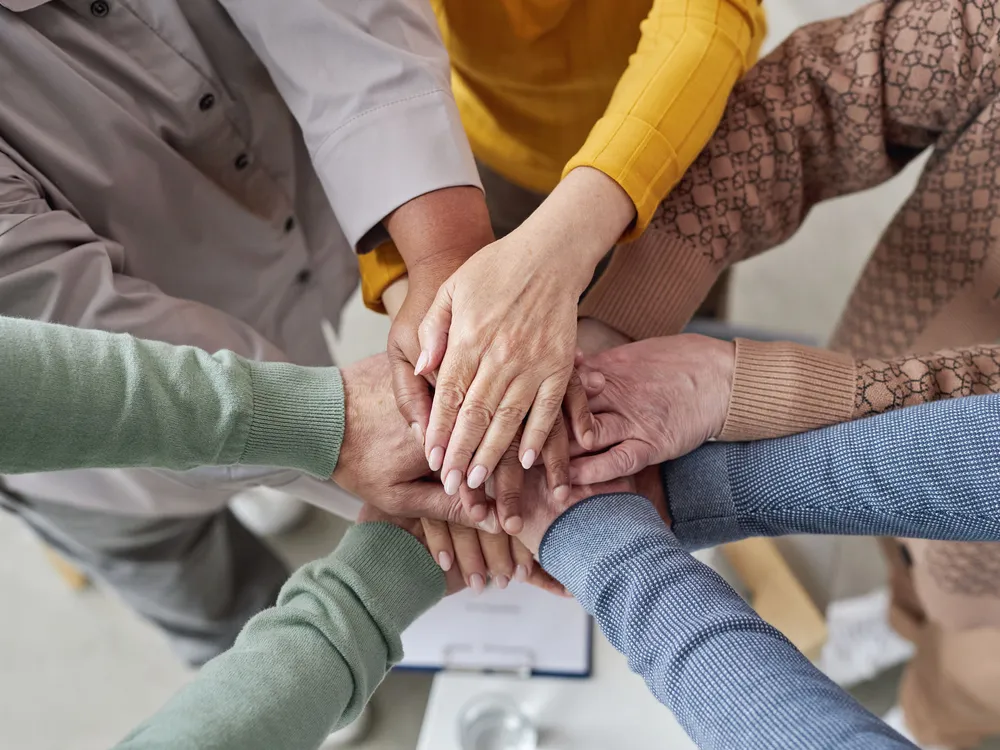 Viele Hände älterer und jüngerer Menschen liegen übereinander – Symbol für Zusammenhalt